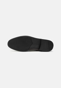 Suela de zapato negra con goma texturizada, con un borde liso y un patrón acanalado para mayor agarre. Diseño minimalista sin acentos adicionales.