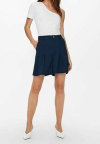 Granatowe spódnicowe szorty z wysokim stanem i pojedynczym przednim guzikiem. Połączone z białym, prążkowanym topem na jedno ramię oraz białymi szpilkami.