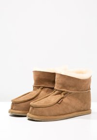 Stivaletti ankle in suede marrone con morbido rivestimento in crema, punta rotonda, lacci laterali e suola in gomma testurizzata. Progettati per comfort e calore.