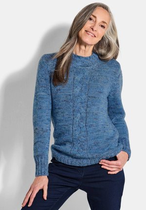 Blauer gestrickter Pullover mit Zopfmuster, Rundhalsausschnitt und gerippten Bündchen. Kombiniert mit dunklen Jeans. Weiche Textur und mittlere Passform.