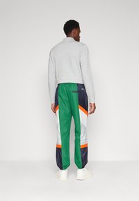 Kleurige trainingsbroek met groene, marineblauwe, witte en oranje panelen. Gemaakt van lichtgewicht materiaal met een elastische tailleband en een achterzak.