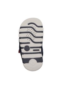 Suela de zapato azul marino con diseño de tracción en goma blanca. Presentaranuras, agujeros de aire y la marca "GEOX". El texto incluye "FLEXY" y "SUAVEMENTE AMORTIGUADO."