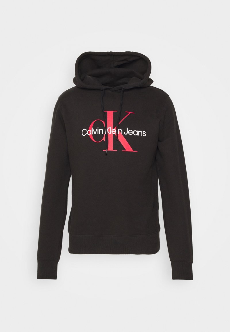 Hoodie noir avec cordons de serrage à l'avant, affichant un grand logo rouge "cK" et "Calvin Klein Jeans" en blanc centré sur la poitrine.