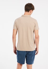 Beige polo shirt met korte mouwen van een zachte stof en een kraag, gecombineerd met blauwe corduroy shorts met twee achterzakken.