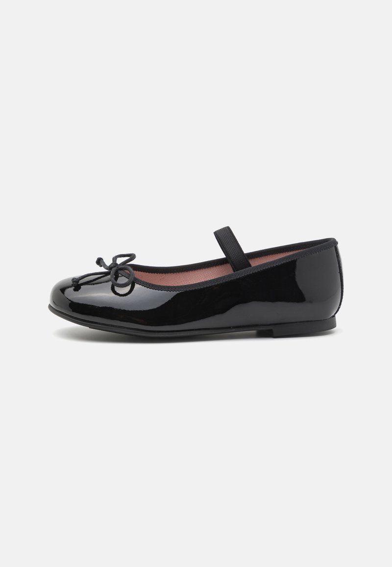 Chaussure plate Mary Jane en cuir verni noir avec un nœud sur l'orteil et une lanière élastique sur le cou-de-pied, vue de profil.