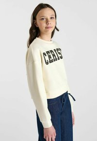 Licht crèmekleurig cropped sweatshirt met een gedurfde zwarte "CERISI" print op de voorkant, gecombineerd met marineblauwe joggers met trekkoord voor een casual look.