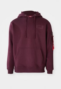 Hoodie bourgogne en tissu doux, avec une poche avant, un capuche à cordon réglable et une poche zippée sur le côté avec un accent de tag rouge.