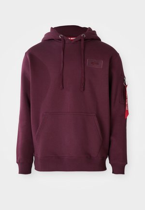 Felpa bordeaux in morbido tessuto, con tasca frontale, cappuccio regolabile con cordino e tasca laterale con zip e particolare etichetta rossa.
