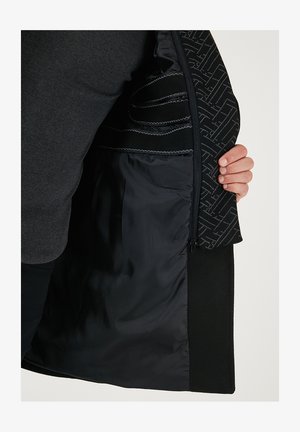 Zwarte jasinterieur met een gladde voering, ingewikkelde patroonaccenten en contrasterende texturen; gesloten met een rits.