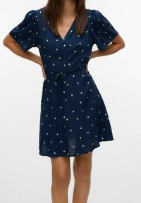 Robe à manches courtes et col en V de couleur bleu marine, avec une patte de boutonnage à l'avant, une ceinture à la taille et un motif de petits pois jaune-vert dispersés. Tissu léger avec une coupe fluide.