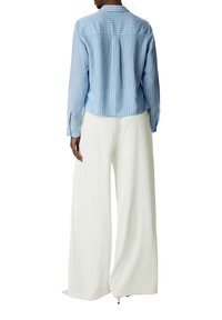 Light blue striped button-up shirt with a back pleat, paired with wide, flowing white pants, featuring a relaxed fit and soft fabric.