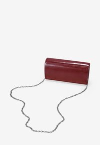 Clutch cilíndrico de cuero rojo con un acabado brillante y una correa de cadena plateada. Presenta un diseño simple y sin costuras con bordes redondeados.