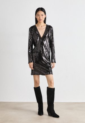 Abito nero in paillettes con maniche lunghe e scollatura a V profonda. Abbinato a stivali neri in morbida pelle scamosciata al ginocchio e una silhouette aderente.