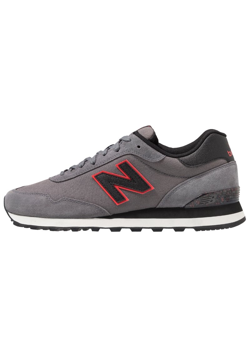 Sneaker grigio con accenti rossi e neri, tomaia in suede e mesh, design con lacci, suola in gomma spessa, presenta un prominente logo "N" sul lato.