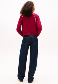 Μπορντό φούτερ με λευκές ραφές, κομμένο στυλ. Σε συνδυασμό με μπλε σκούρο τζιν παντελόνι με φαρδιά μπατζάκια, πίσω τσέπες και ελαφριά ξεθωριάσματα.