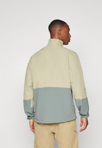 Leichte Jacke mit hohem Kragen, bestehend aus einem oberen Teil in Beige und einem strukturierten, hellblauen unteren Teil. Elastische Bündchen und Saum.
