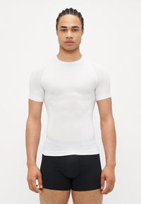 White short-sleeve tight-fitting athletic shirt, made of smooth fabric, featuring a textured panel on the chest, paired with black shorts.