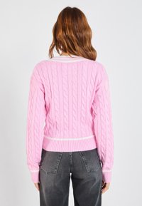 Cable-knit trui in lichtroze met contrasterende witte geribbelde tailleband en manchetten. Heeft lange mouwen en een relaxte pasvorm.