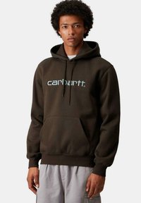 Sudadera marrón con bolsillo frontal, capucha con cordón ajustable y logo "carhartt" en azul claro. Fabricada con un tejido suave y de corte relajado.