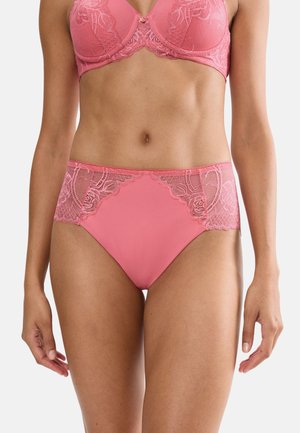Donna che indossa un reggiseno in pizzo rosa abbinato a mutandine a vita alta, con evidenza della zona addominale e della parte superiore delle cosce su sfondo bianco.