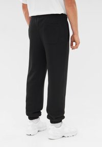 Zwarte sweatpants met een elastische tailleband, geribbelde boorden en een enkele achterzak. Draagt met witte sportschoenen. Eenvoudig, casual ontwerp.