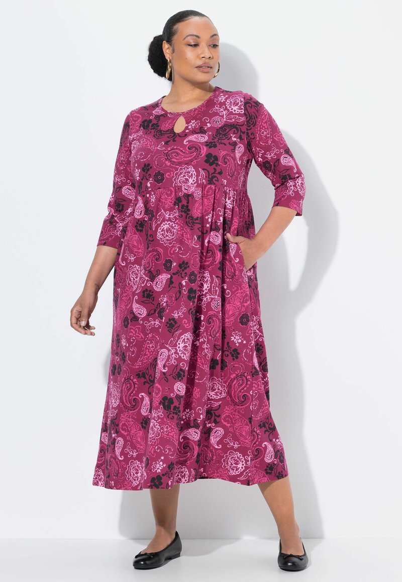 Langes, fließendes Kleid in tiefem Pink mit schwarz-weißen Blumenmustern. Besitzt einen runden Halsausschnitt mit einem Schlüssel-ausschnitt und Dreiviertelärmel.