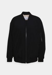 Veste bomber noire avec fermeture éclair frontale, poignets côtelés et une seule poche zippée sur la manche. Fabriquée en tissu léger avec une texture lisse.