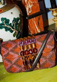 Borsa a mano con perline caratterizzata da un design multicolore in arancione, rosa e viola. Decorata con grandi perline colorate sulla parte frontale e dotata di tracolla in pelle.