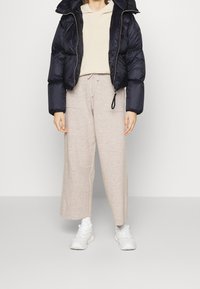 Marineblå pufferjakke, beige strikket sweater og lysebrune bredbenede bukser, parret med hvide sneakers. Strukturerede materialer.