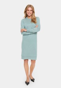 Ljus teal klänning med lång ärm, ribbade ärmslut och fåll. Styling med svarta spetsiga ballerinas. Slät textur.