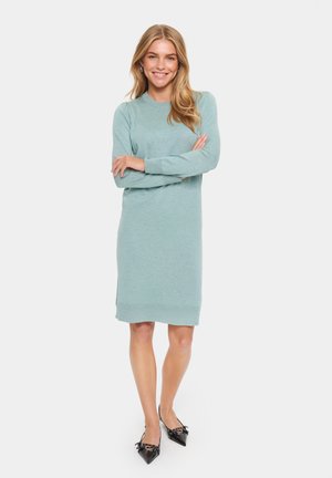 Helles Türkisfarbiges Strickkleid mit langen Ärmeln, gerippten Manschetten und Saum. Stylisch kombiniert mit schwarzen spitzen Ballerinas. Glatte Textur.