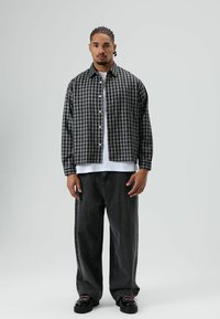 Zwart-wit geruit flanellen overhemd met knopen aan de voorkant, gedragen over een wit T-shirt, gecombineerd met wijde donkere spijkerbroeken en zwarte schoenen.