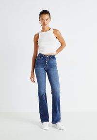 Hvid ribbet crop top parret med højtsiddende blå flared jeans med knaplukning og fem lomme-design, kompletteret med hvide sneakers.