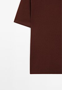 T-shirt z krótkim rękawem w kolorze bordowym, wykonany z bawełny. Posiada okrągły dekolt oraz gładką teksturę z czystym szwem przy rękawach i brzegu.