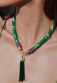 Choker en tissu vert avec un motif floral, accessoires en métal doré, embellissements en perles colorées et un pendentif à franges vert.