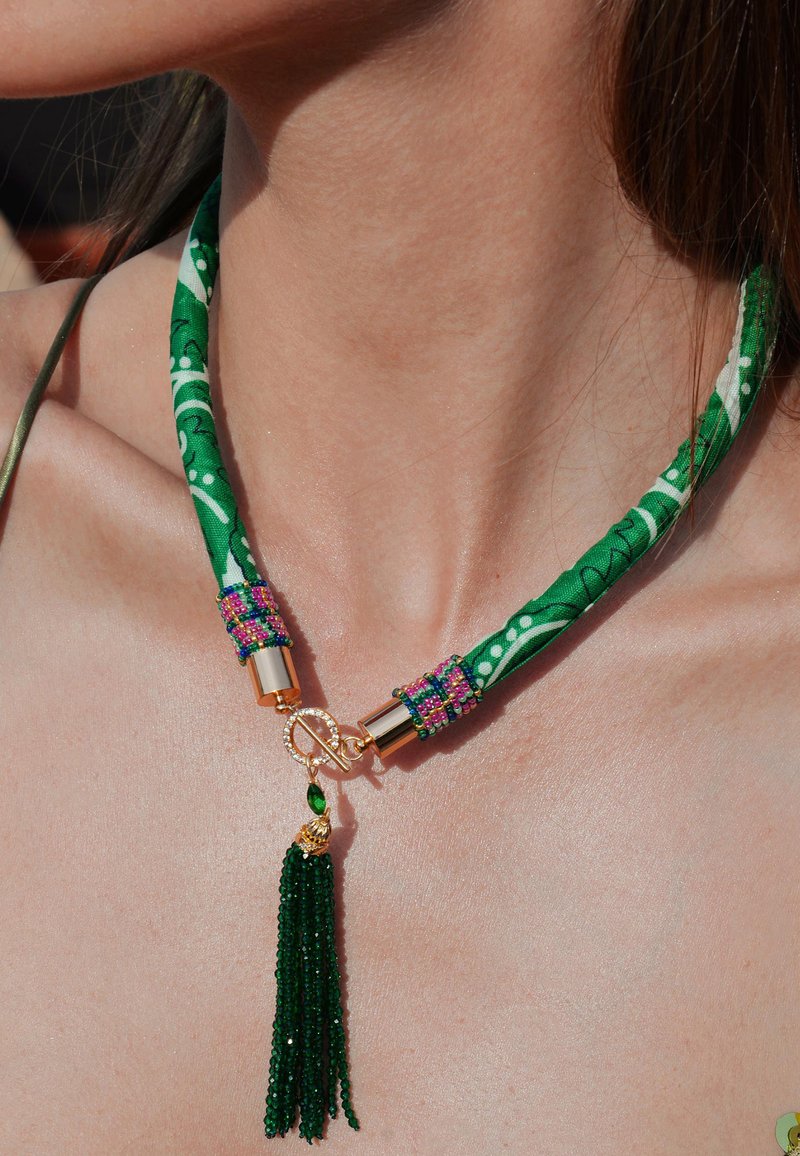 Choker en tissu vert avec un motif floral, accessoires en métal doré, embellissements en perles colorées et un pendentif à franges vert.