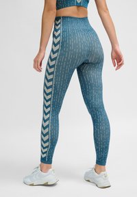 Strumpbyxor i en teal-färg med vertikala och diagonala linjemönster. Hög midja med en kontrasterande chevronrand längs sidan.