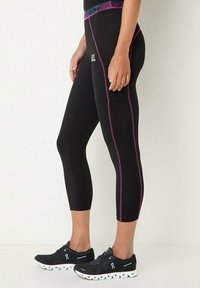 Leggings sportivi neri con texture a coste, cuciture a contrasto viola e una cintura larga. Abbinati a sneakers nere con suole bianche.