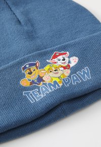 Gorro de punto azul con un gráfico de tres perros de dibujos animados con varios acentos de color, junto con el texto "EQUIPO PAW" en blanco.