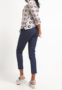 Flerfärgad blommig skjorta med trekvartsärmar, marinblå smalbyxor och vita platåsandaler med grå och svart design.