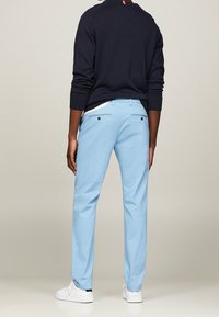 Błękitne spodnie o prostym kroju, wykonane z teksturowanej tkaniny, z dwiema tylnymi kieszeniami i wąskim paskiem w talii. W zestawie z białymi sneakersami i ciemnym topem.