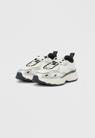 Λευκά και γκρι αθλητικά παπούτσια με χοντρή σόλα, υφή υφάσματος, μαύρες πινελιές και αντίθετα κορδόνια. Κωνικό σχήμα με έλξη στο πίσω μέρος του τακουνιού.