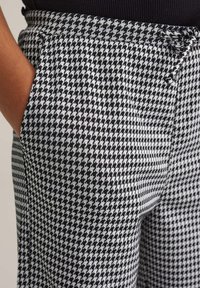 Hlače s črno-belo houndstooth vzorcem, sproščenega kroja, z žepi, z vrvico za zategovanje in teksturirano tkanino.