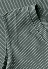 Gros plan sur deux morceaux de tissu vert rayé, montrant un décolleté en V et des détails de manches, mettant en avant la texture et le motif.