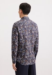 Langsleeve shirt met een donker bloemenpatroon met blauwe, bruine en witte bloemen. Gekleed ontwerp met een ronde onderkant.