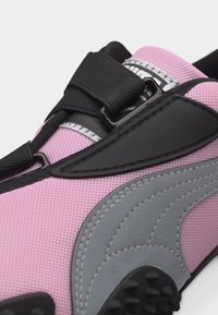 Κοντινό πλάνο ροζ αθλητικού παπουτσιού με γκρι λεπτομέρειες, μαύρο ιμάντα με βέλκρο και υφή στη σόλα για καλύτερη πρόσφυση.