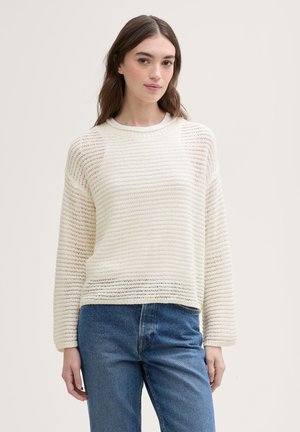 Hellbeige gestrickter Pullover mit horizontalen Streifen, Rundhals-Ausschnitt, lockerer Passform und gerippten Bündchen, kombiniert mit blauen High-Waist-Jeans.