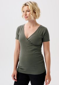 Oliven grøn kortærmet top med dyb V-udskæring og sammenfoldet sidesyning, lavet af ribbet stof, tætsiddende design, parret med sorte jeans.