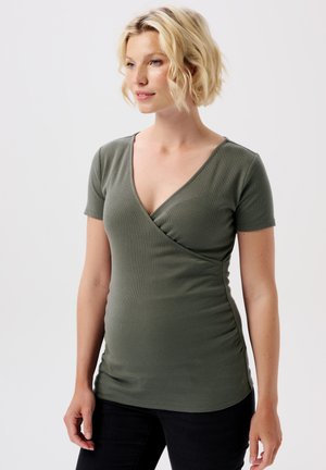 Olivgrünes Kurzarmoberteil mit tiefem V-Ausschnitt und gerafftem seitlichen Detail, aus geripptem Stoff, taillierter Passform, kombiniert mit schwarzen Jeans.