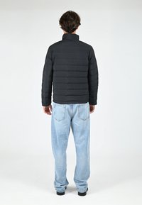 Doudoune noire avec un col montant, présentant des motifs matelassés horizontaux. Associée à un jean bleu clair, ample.